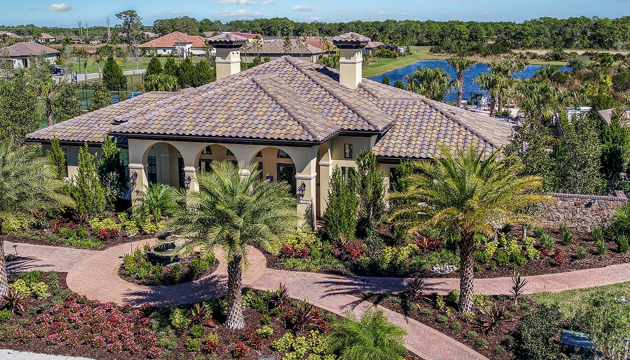 Aerial view of a Mediterranean-style clubhouse with lush tropical landscape and lakefront golf course