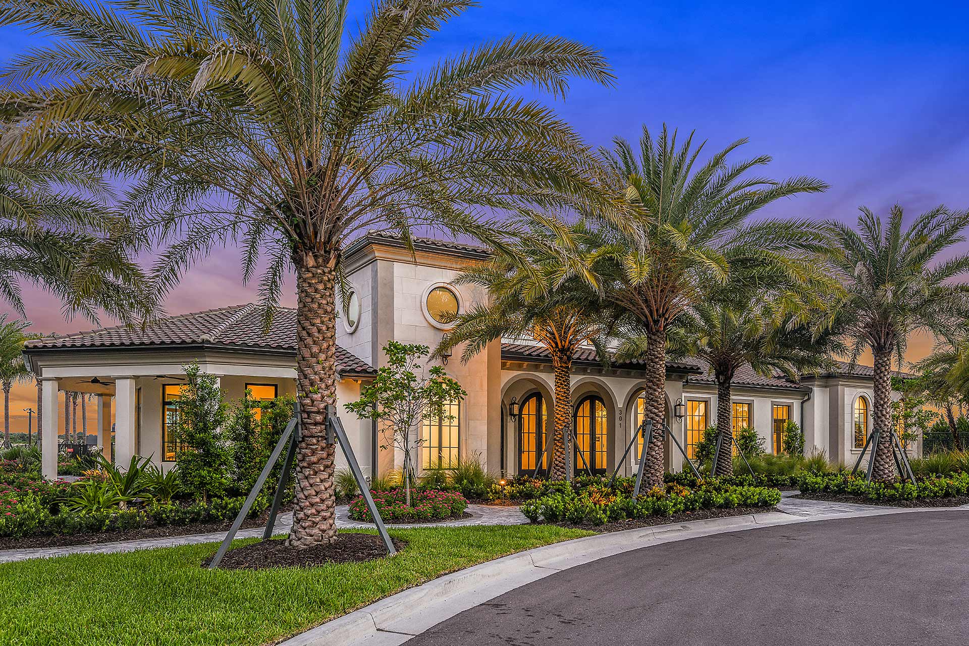Club Aria clubhouse at twilight with layered palms and lush foundation planting